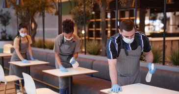 Portrait of workers wearing masks in row while cleaning tables in cafe interior, covid safety concept, copy space